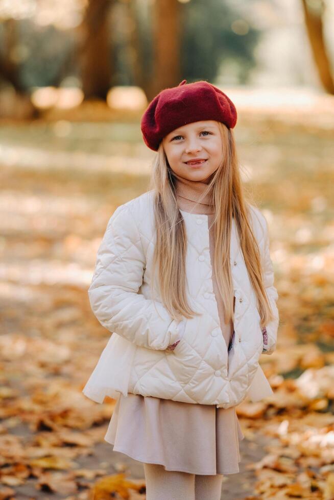 un contento niña en un gorra caminando en el otoño parque foto