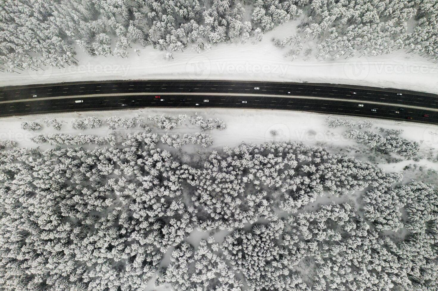 View from the height of the winter forest with snow-covered trees in winter and a forest road with cars photo