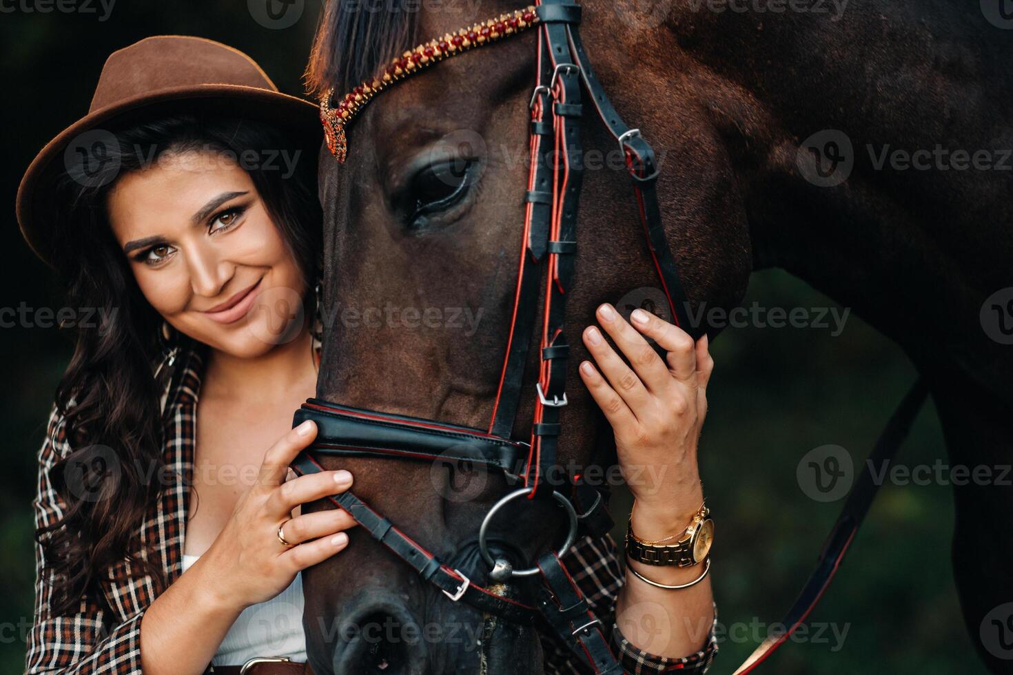 pregnant girl with a big belly in a hat next to horses in the forest in nature.Stylish girl in white clothes and a brown jacket. photo