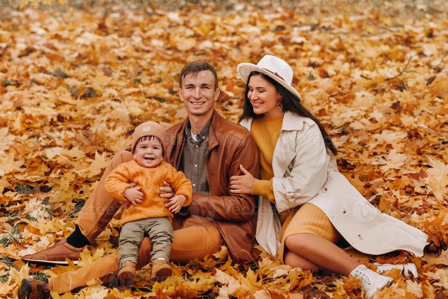 Father and mother with son sitting in the autumn Park. Portrait of a Golden autumn Family in a nature Park. photo