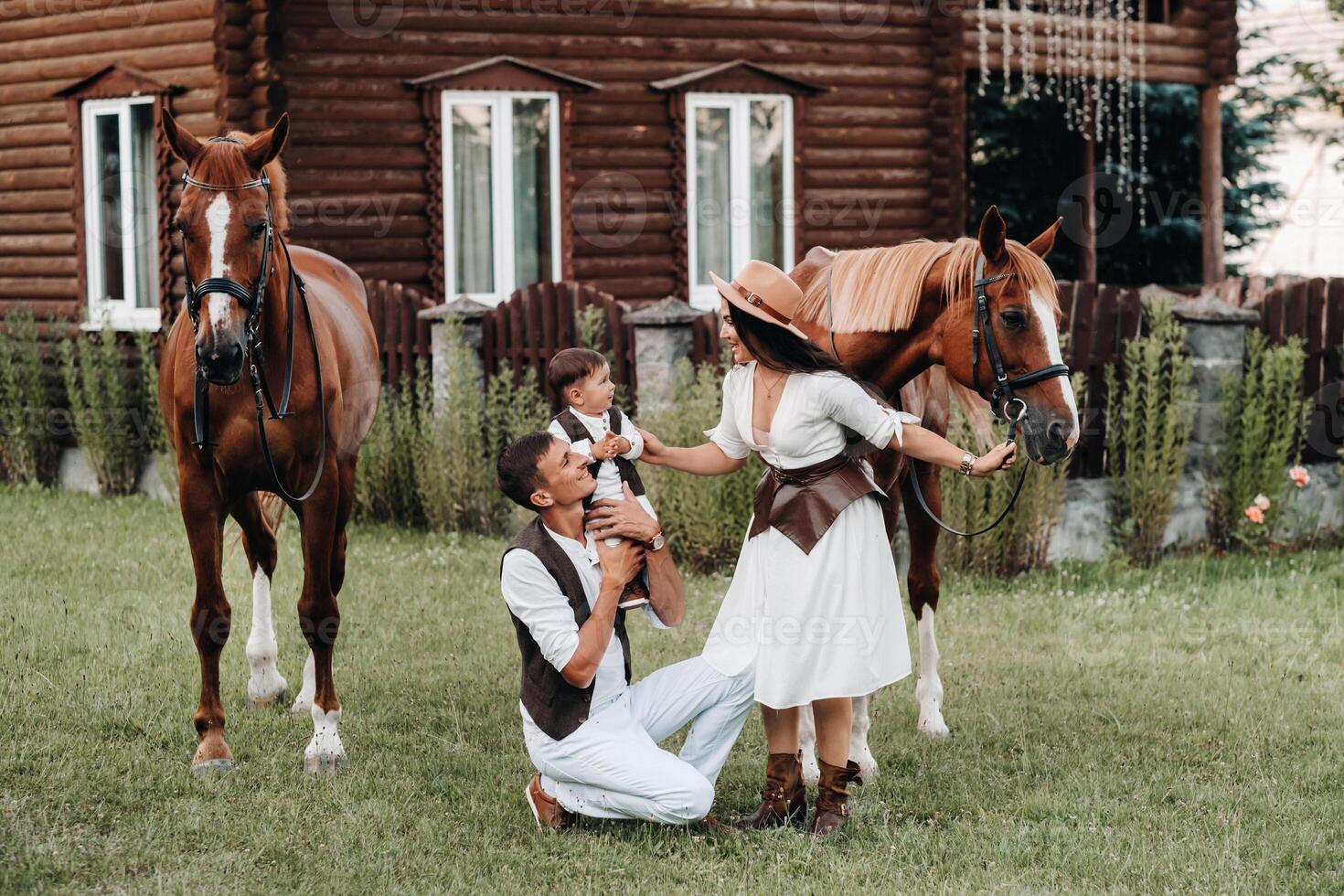 A family in white clothes with their son stand near two beautiful horses in nature. A stylish couple with a child are photographed with horses photo