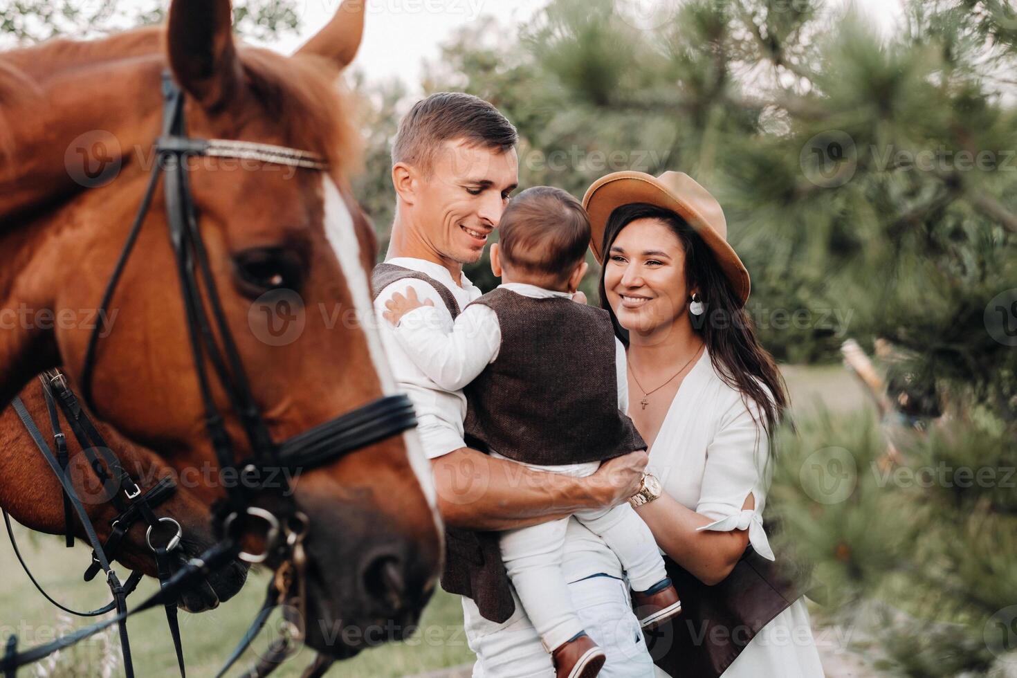 A family in white clothes with their son stand near two beautiful horses in nature. A stylish couple with a child are photographed with horses photo