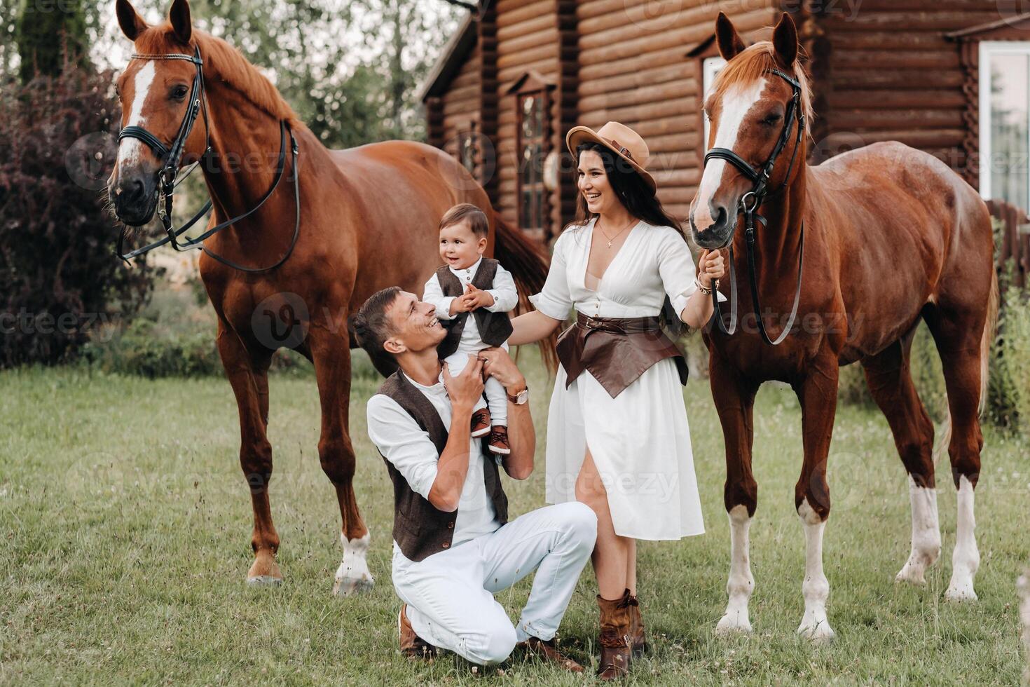 A family in white clothes with their son stand near two beautiful horses in nature. A stylish couple with a child are photographed with horses photo