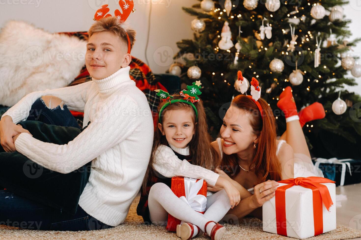 a happy family is lying on the floor of the house with New Year's gifts, next to the Christmas tree photo