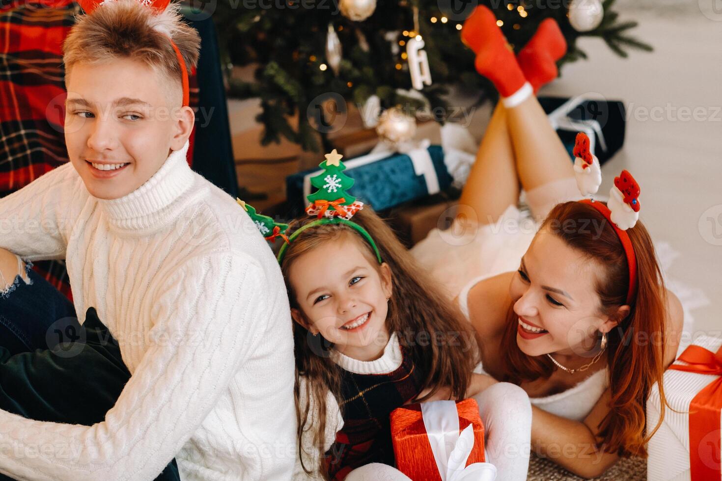 a happy family is lying on the floor of the house with New Year's gifts, next to the Christmas tree photo
