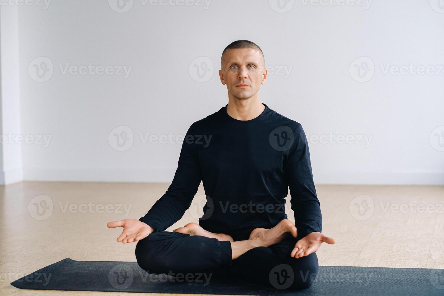 Portrait of an adult athletic man sitting in the lotus position in the gym on the mat photo