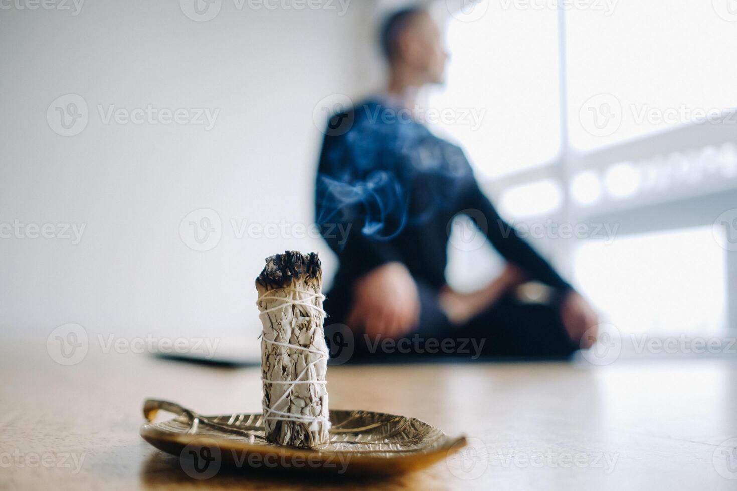 A male athlete in black sportswear sits in the lotus position against the background of an incense candle in the gym. photo