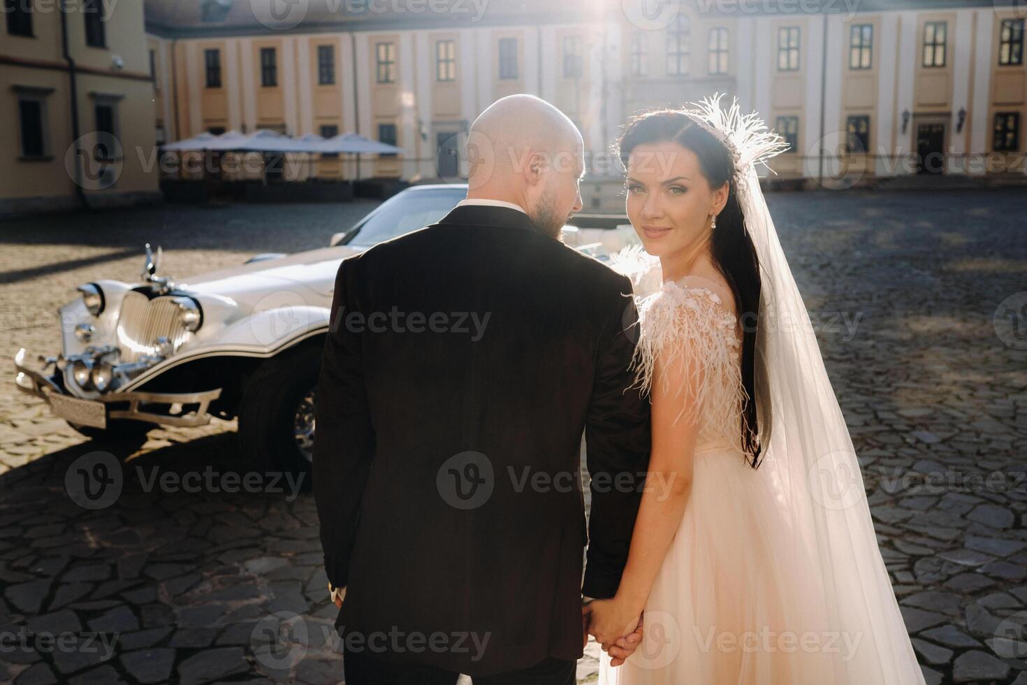An elegant wedding couple In the courtyard of the castle walks holding hands near a retro car photo
