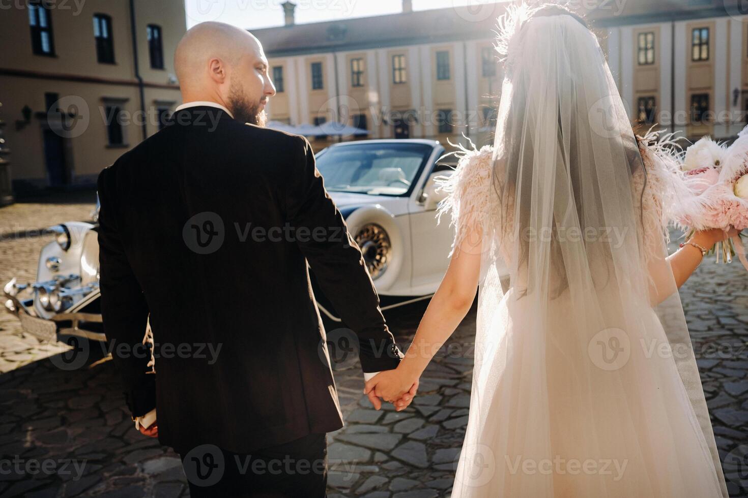 An elegant wedding couple In the courtyard of the castle walks holding hands near a retro car photo