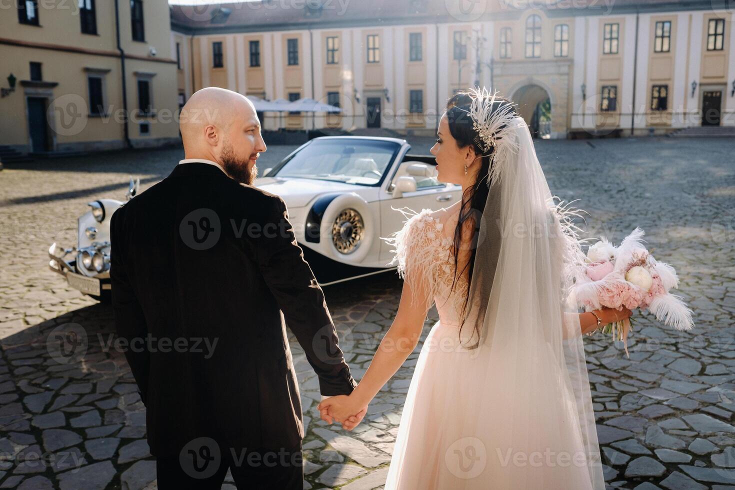 An elegant wedding couple In the courtyard of the castle walks holding hands near a retro car photo