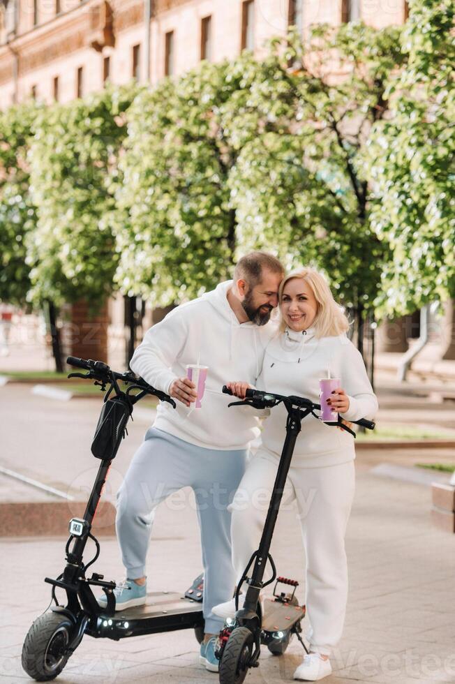 A couple in love in white clothes stands in the city on electric scooters with a drink in their hands photo
