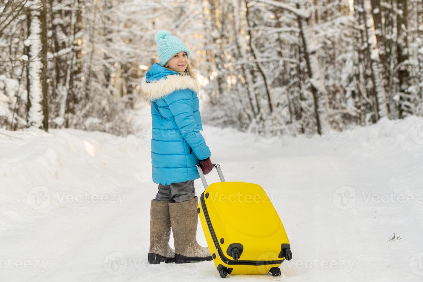 A girl in winter in felt boots goes with a suitcase on a frosty snowy day photo
