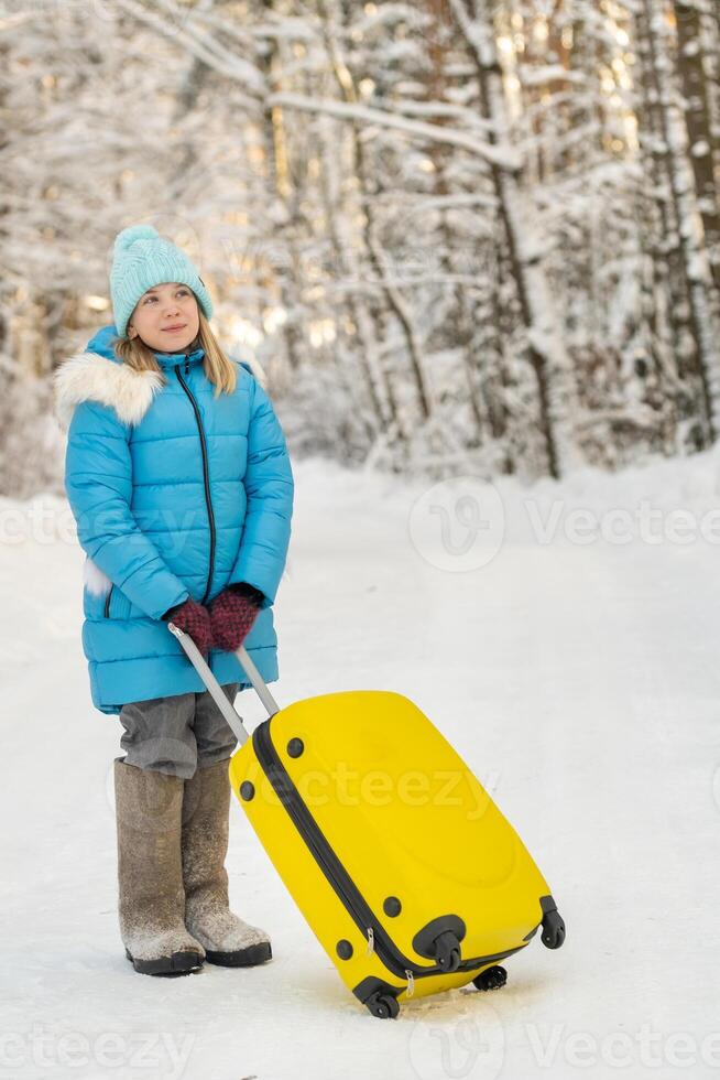 A girl in winter in felt boots goes with a suitcase on a frosty snowy day photo