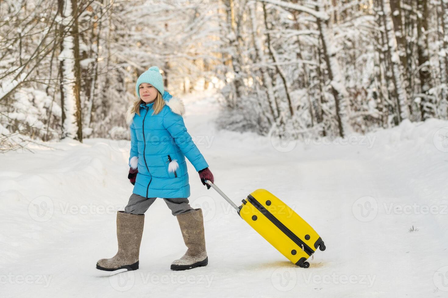 A girl in winter in felt boots goes with a suitcase on a frosty snowy day photo