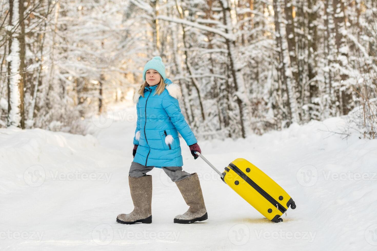 A girl in winter in felt boots goes with a suitcase on a frosty snowy day photo