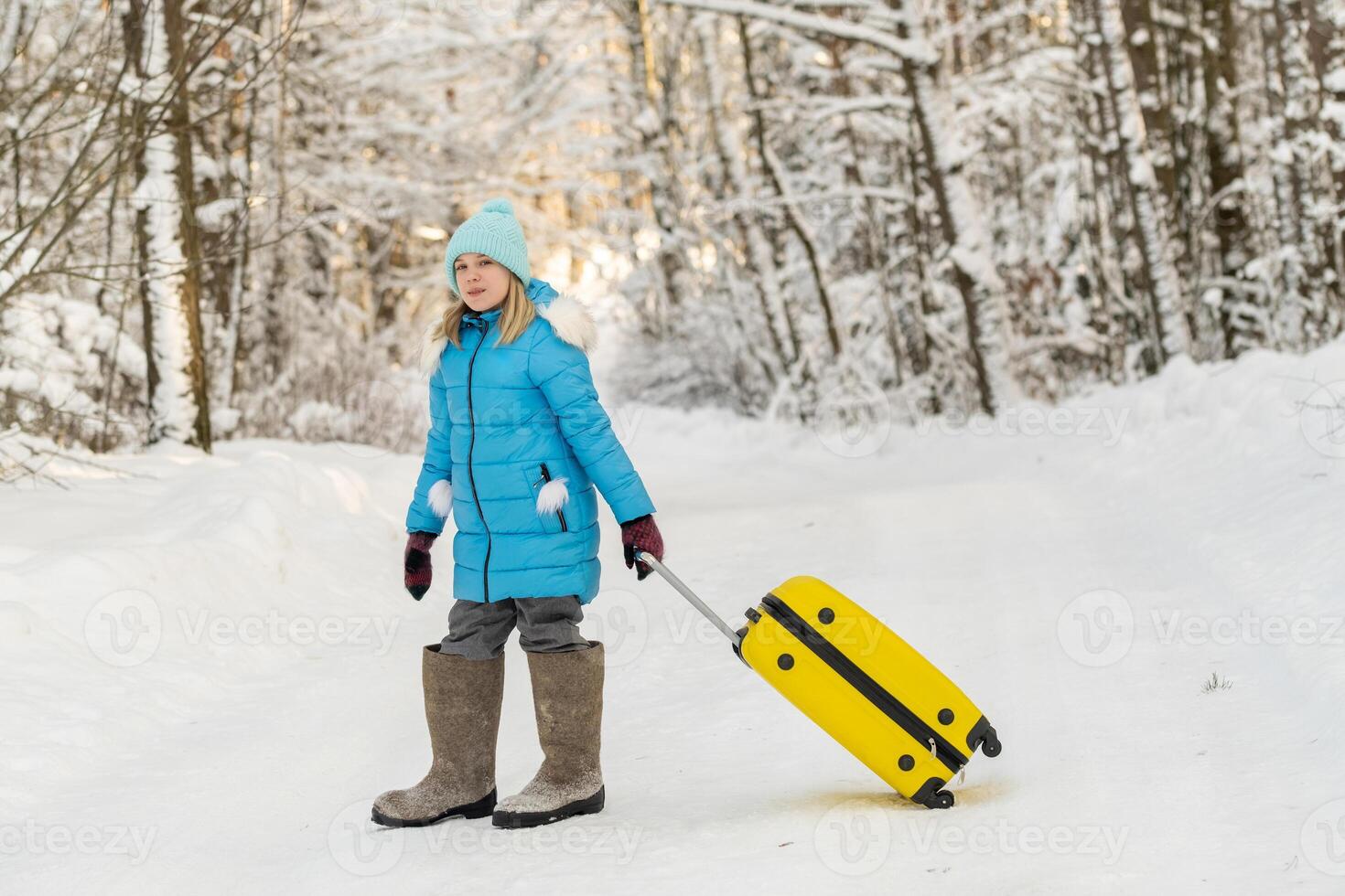 A girl in winter in felt boots goes with a suitcase on a frosty snowy day photo