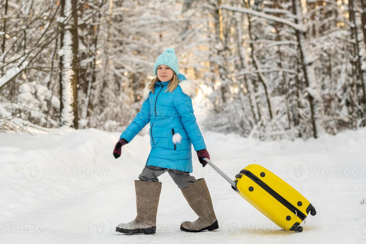 A girl in winter in felt boots goes with a suitcase on a frosty snowy day photo
