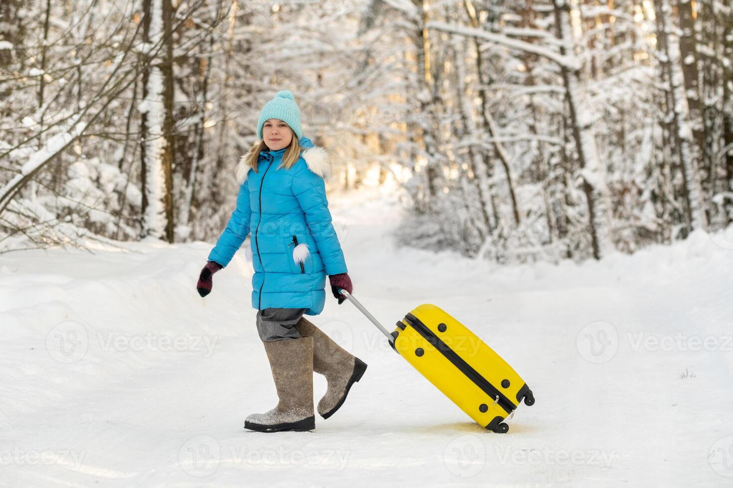 A girl in winter in felt boots goes with a suitcase on a frosty snowy day photo