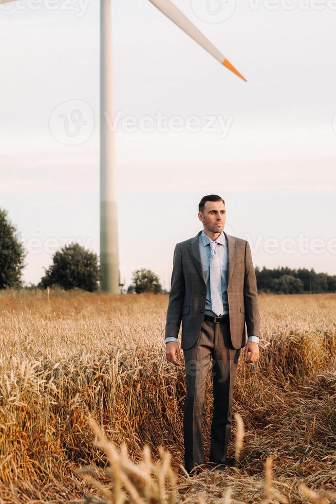 Portrait of a businessman in a gray suit on a wheat field against the background of a windmill and the evening sky photo