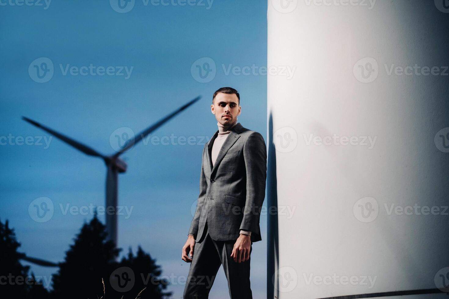 A man in a grey business suit stands next to a windmill after sunset .Businessman near windmills at night.Modern concept of the future. photo