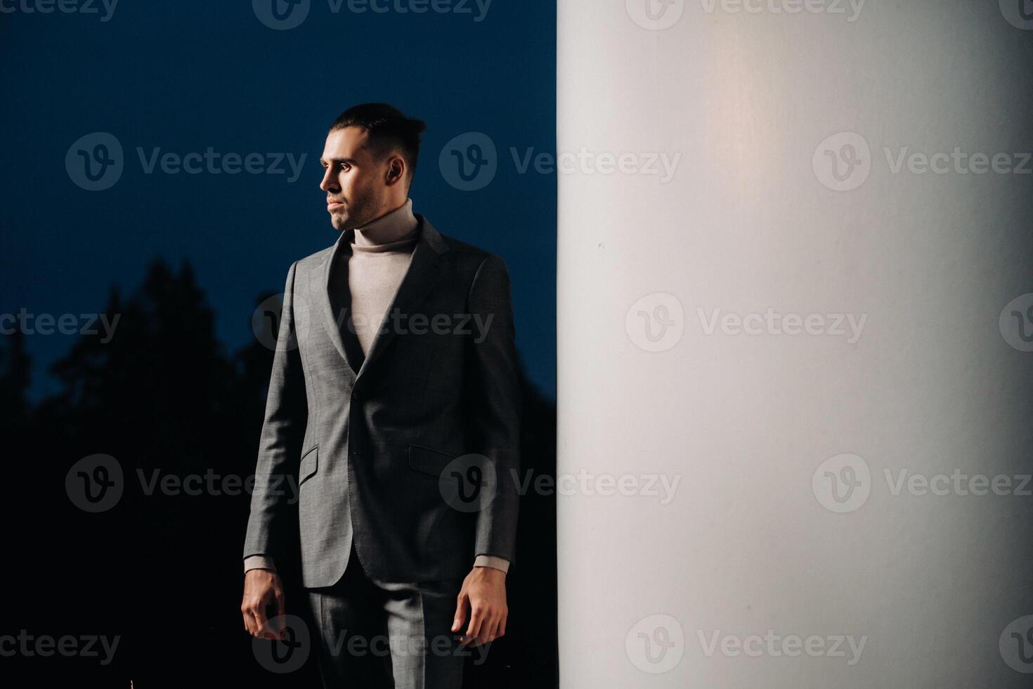 A man in a grey business suit stands next to a windmill after sunset .Businessman near windmills at night.Modern concept of the future. photo