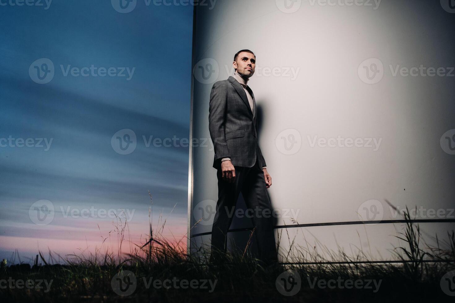 A man in a grey business suit stands next to a windmill after sunset .Businessman near windmills at night.Modern concept of the future. photo
