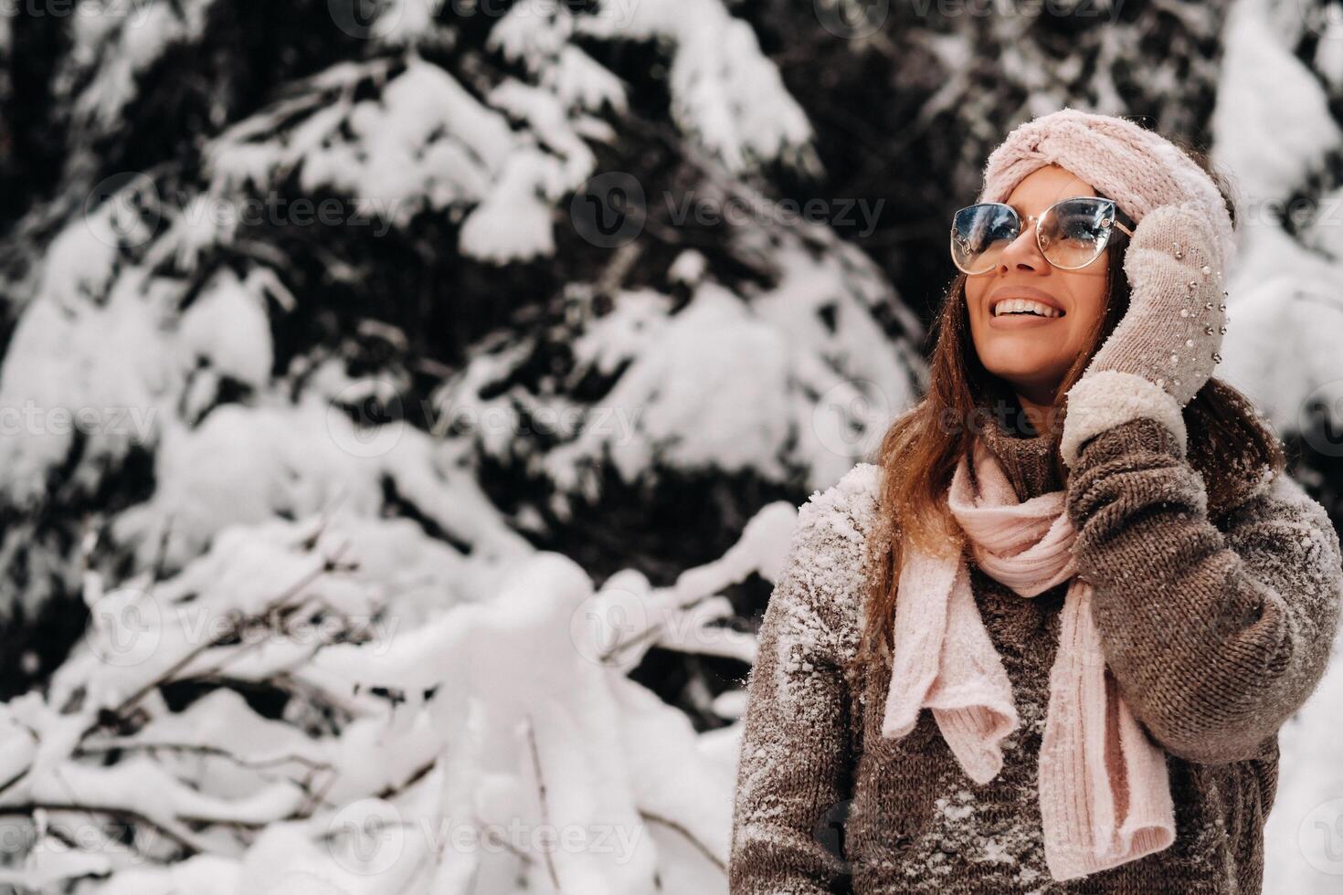 A girl in a sweater and glasses in winter in a snow-covered forest photo