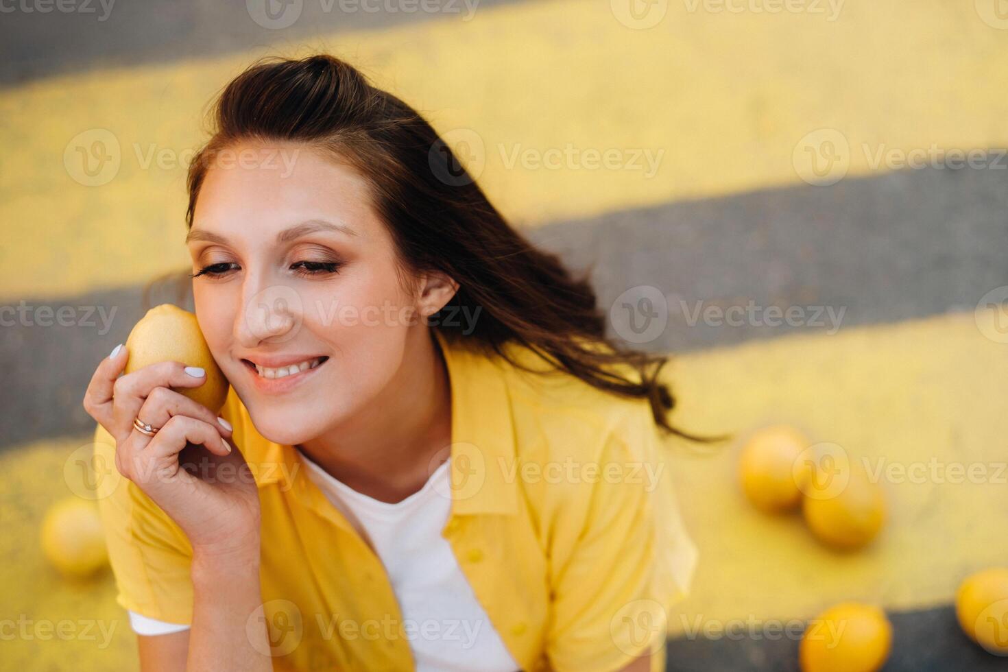 a girl with lemons in a yellow shirt, shorts and black shoes sits on a yellow pedestrian crossing in the city. The lemon mood photo
