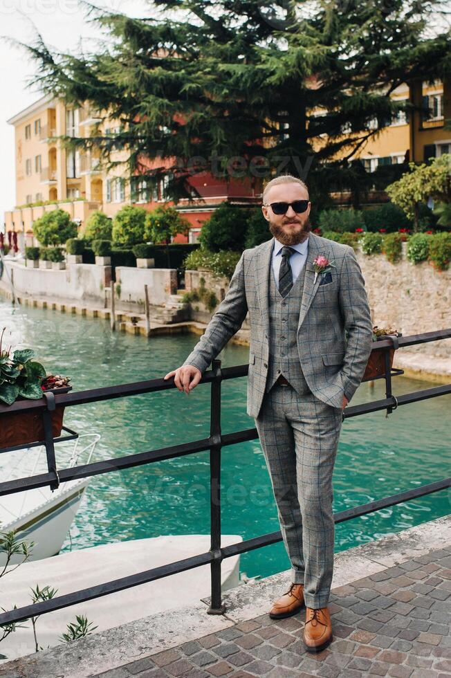 A man with a beard in a strict grey three-piece suit with a tie in the old town of Sirmione, a Stylish man in a grey suit in Italy photo