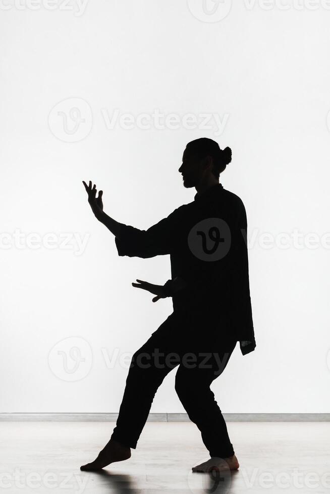 Silhouette of a person practicing qigong energy exercises on a light background photo