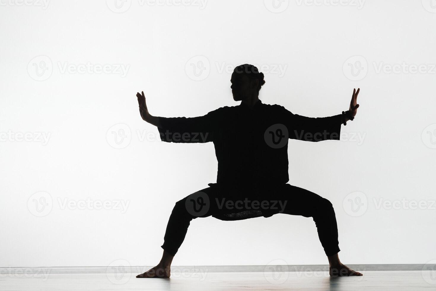 Silhouette of a person practicing qigong energy exercises on a light background photo