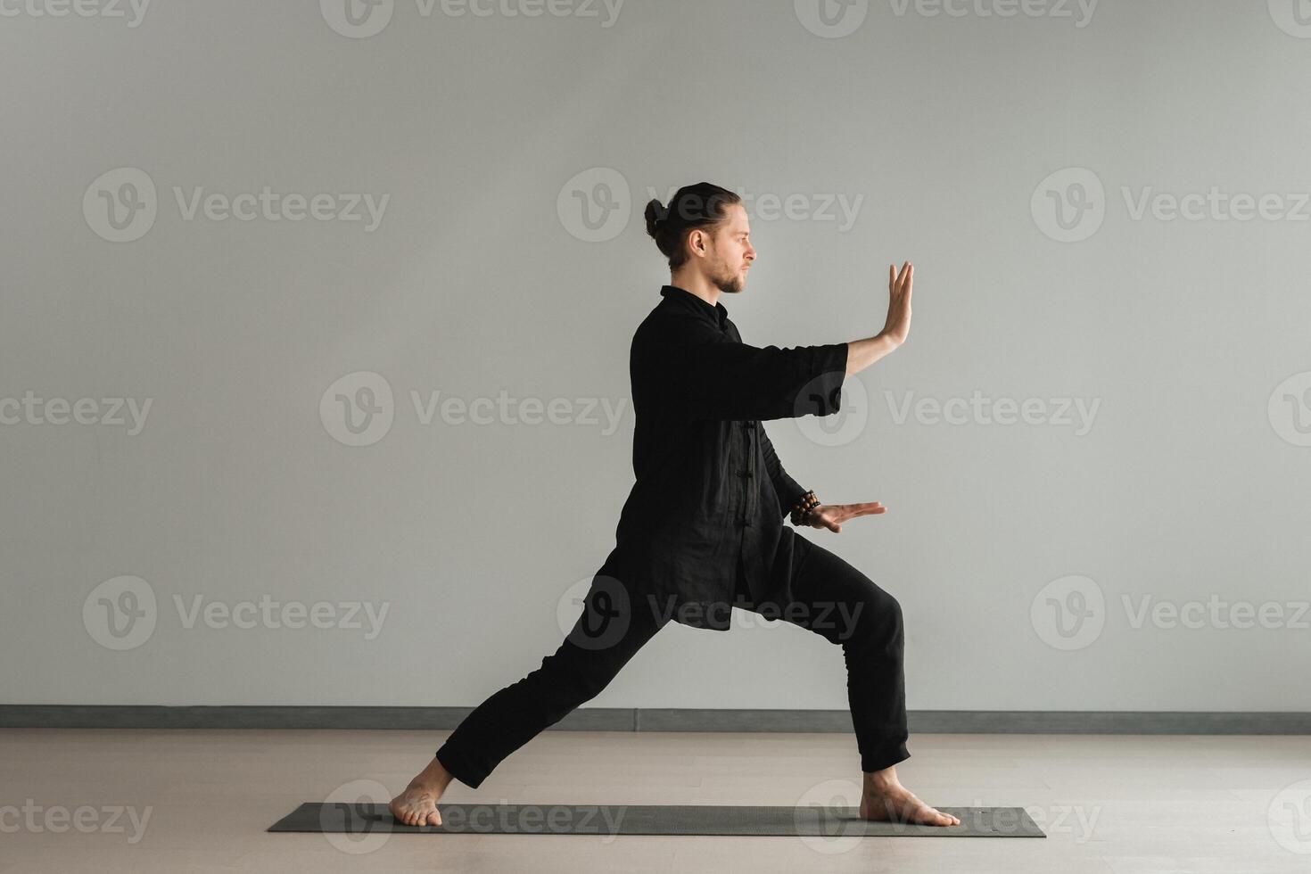 A man in black kimano practicing qigong energy exercises indoors photo