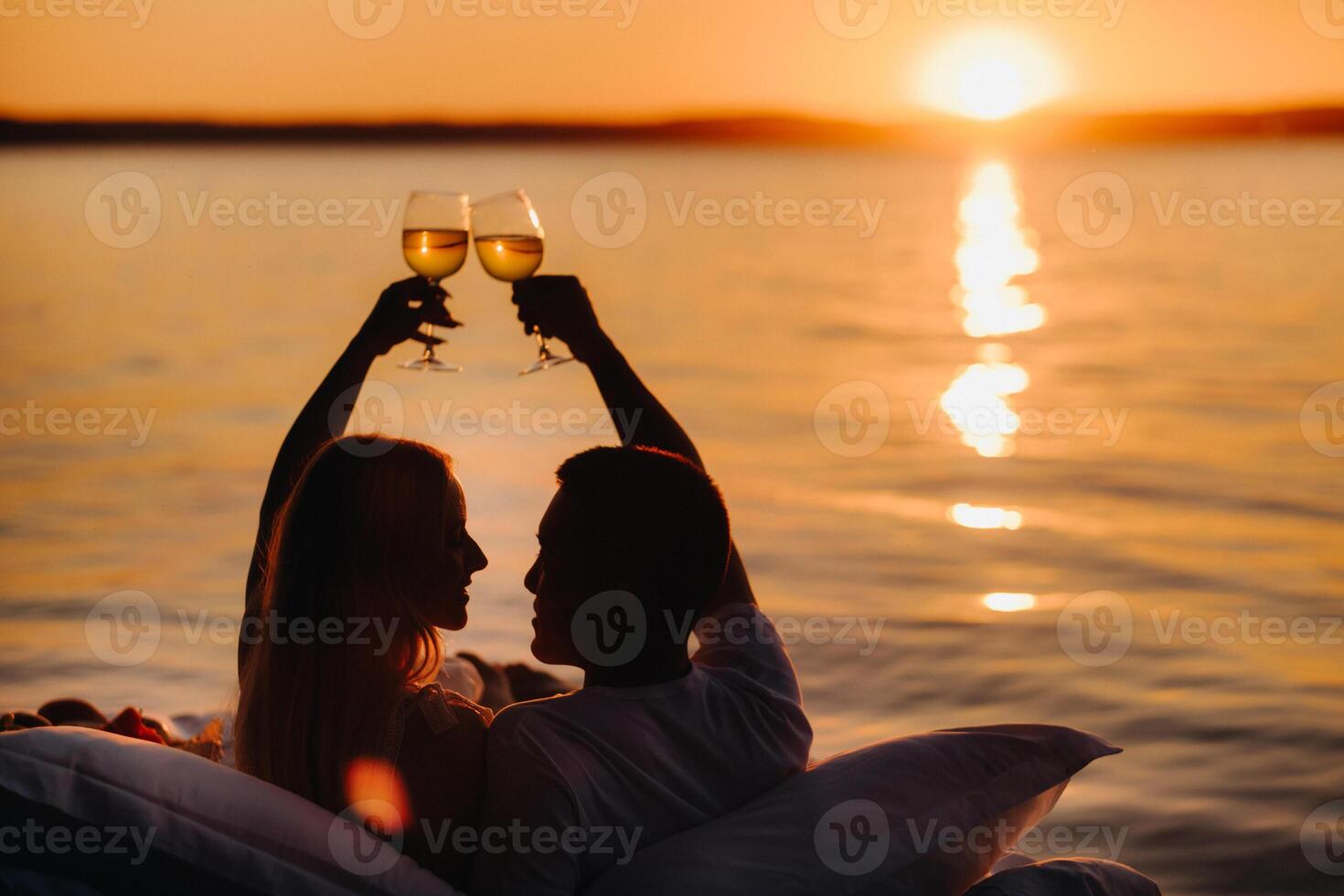 Silhouettes of a happy couple raising glasses on a summer evening near the sea at sunset photo