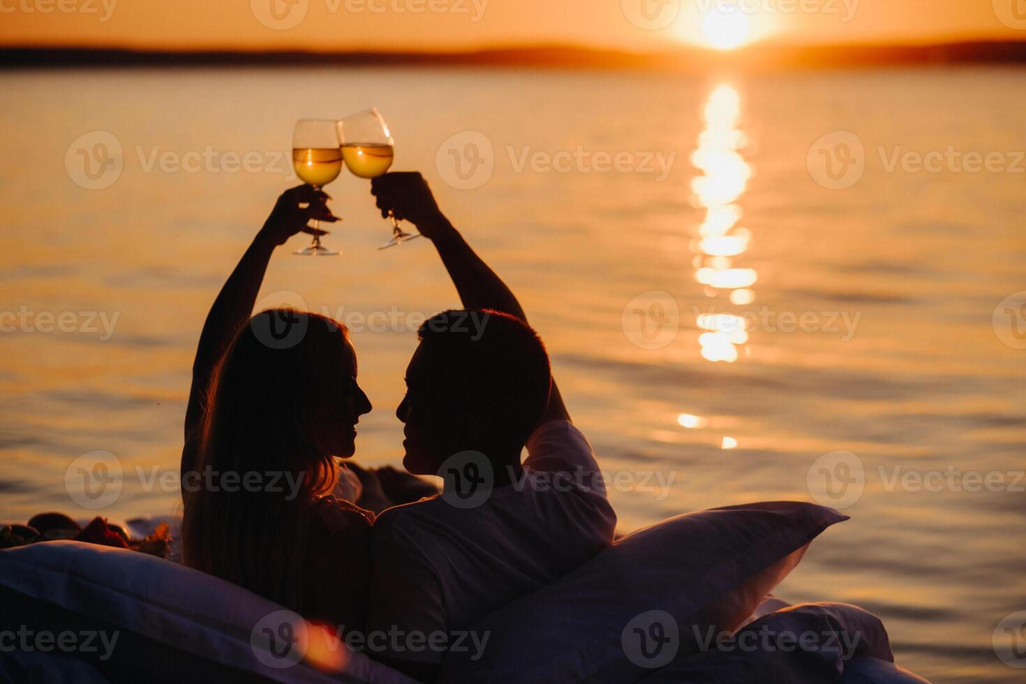 Silhouettes of a happy couple raising glasses on a summer evening near the sea at sunset photo