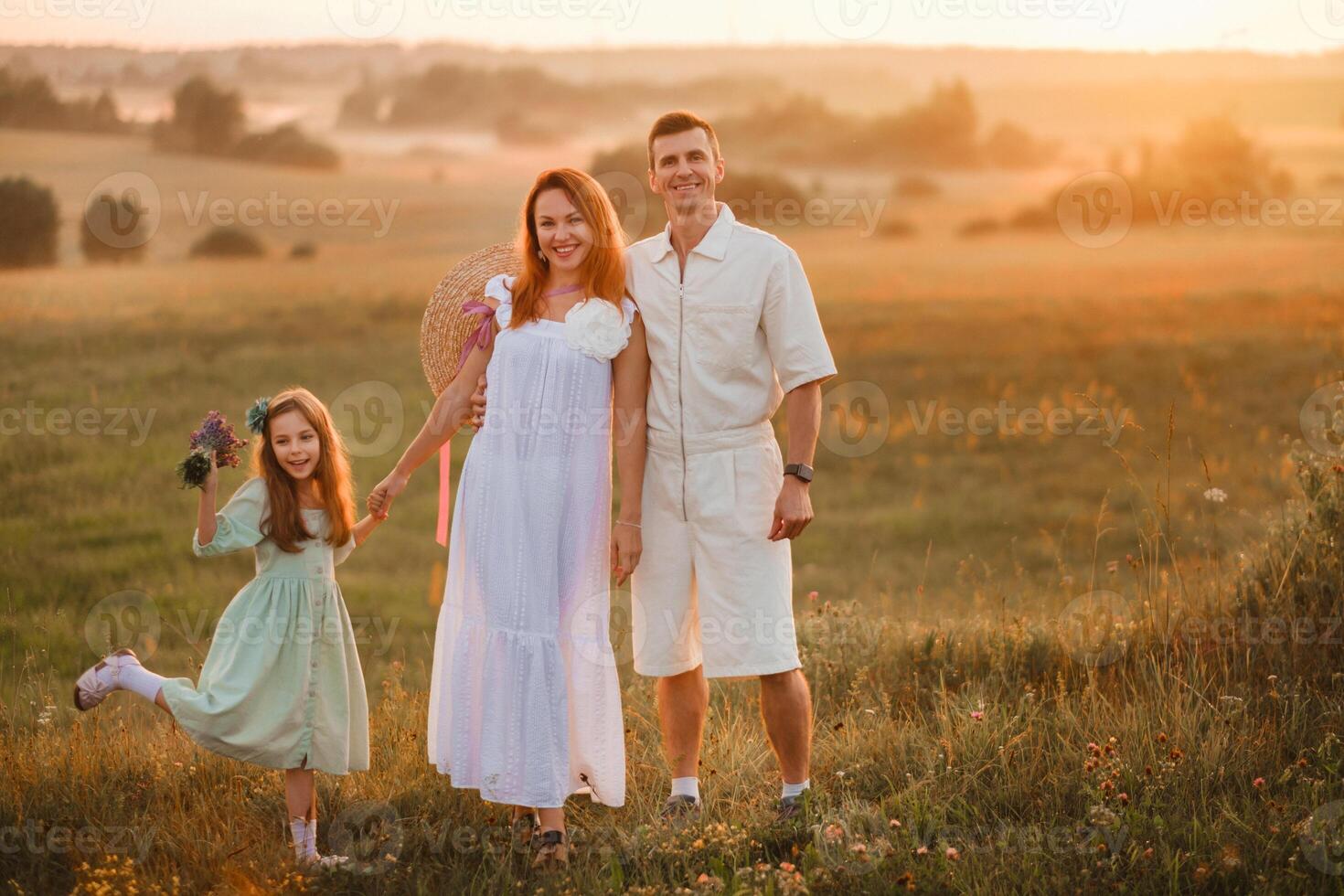 A beautiful happy family of three is standing in a field at sunset photo