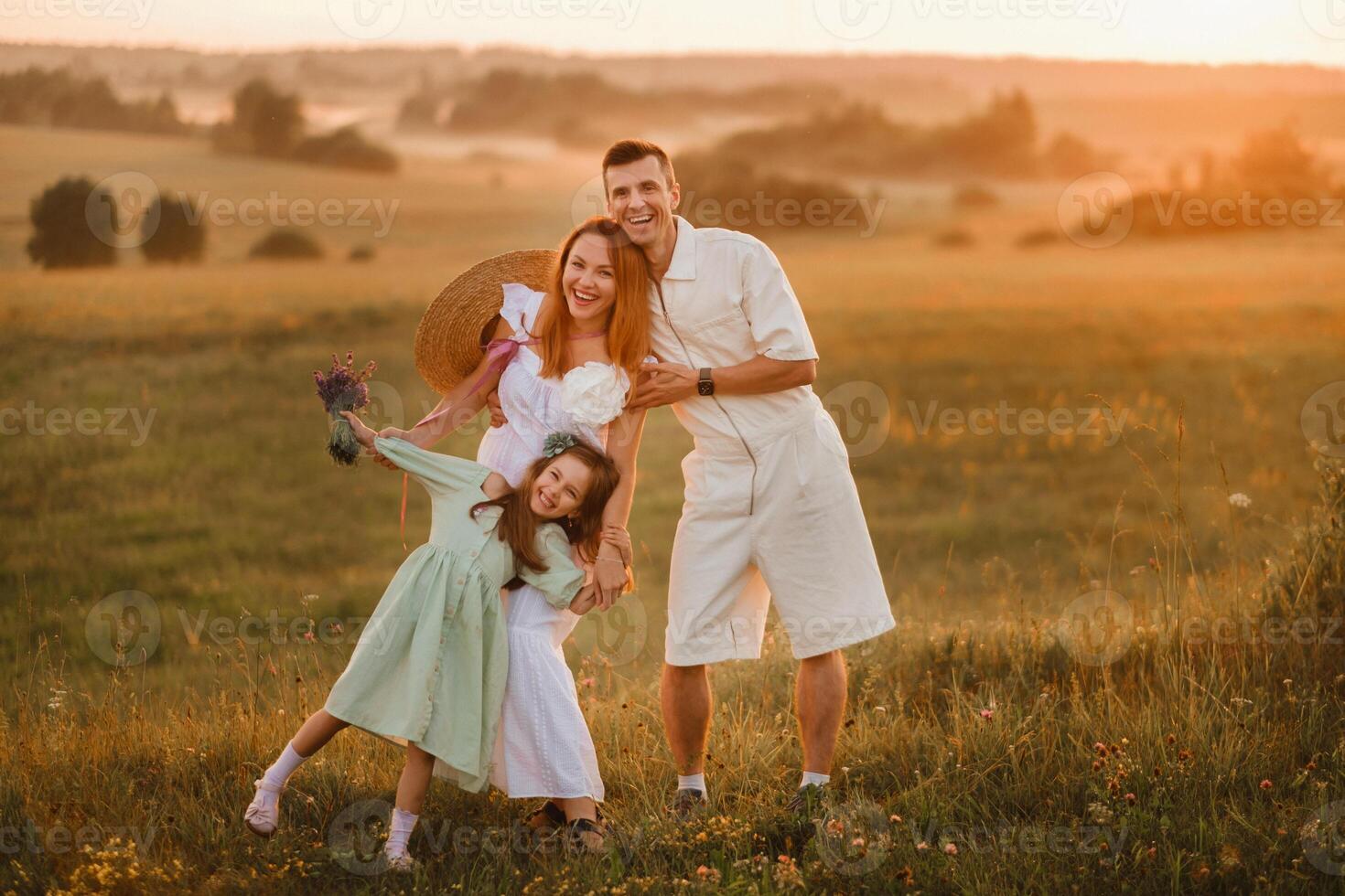 A beautiful happy family of three is standing in a field at sunset photo