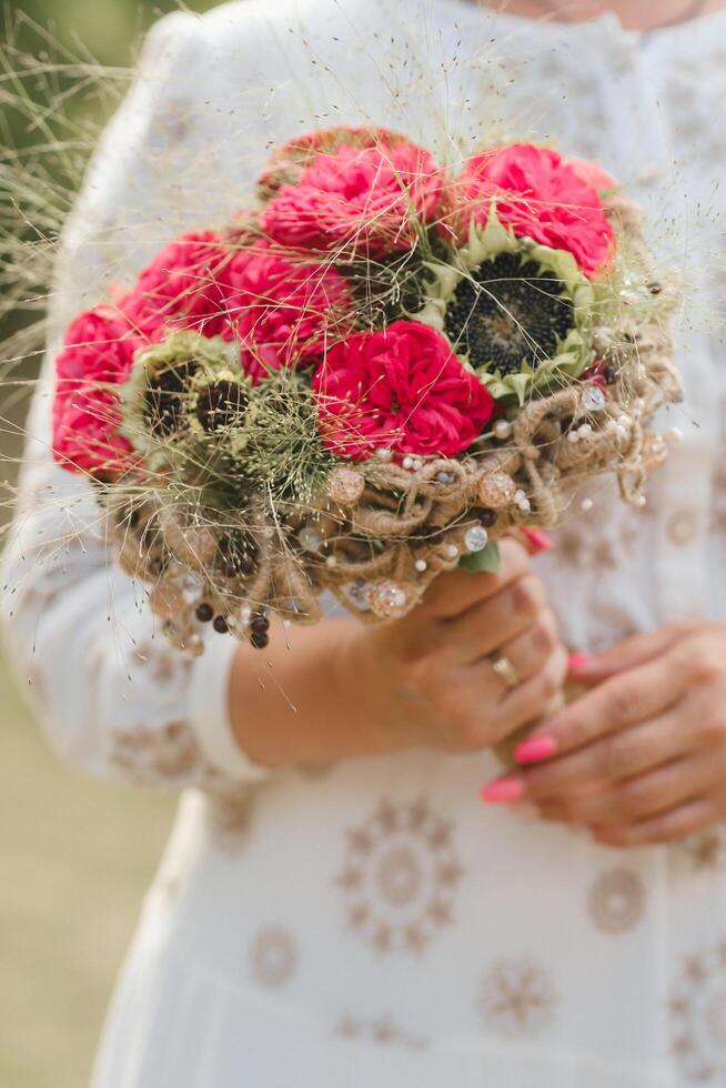 The bride holds her wedding bouquet with red peonies and sunflowers in her hands photo