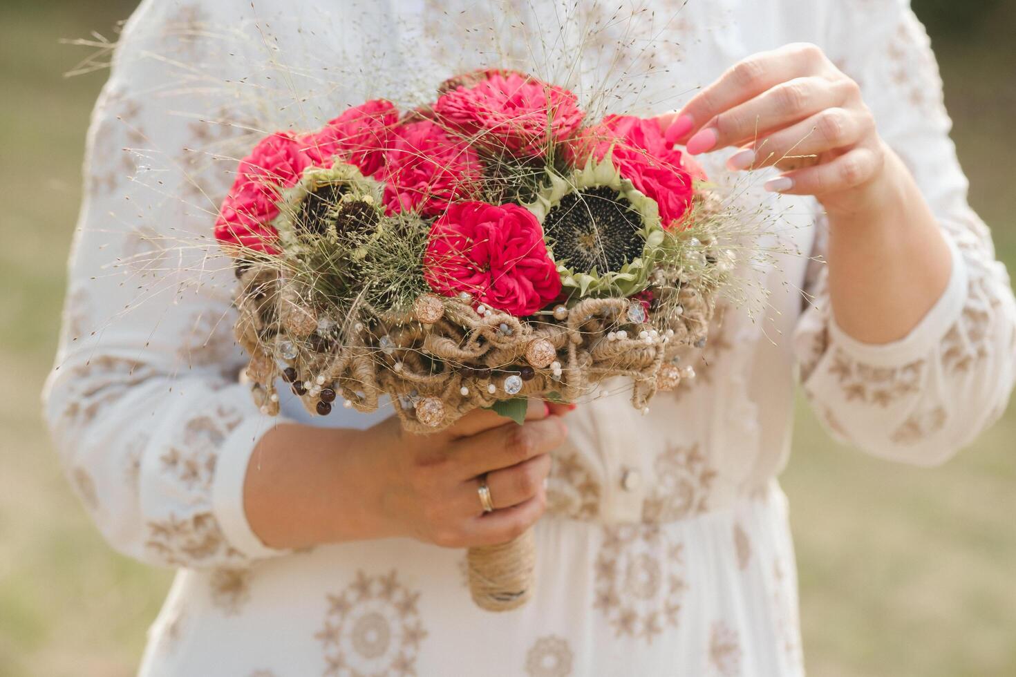 The bride holds her wedding bouquet with red peonies and sunflowers in her hands photo