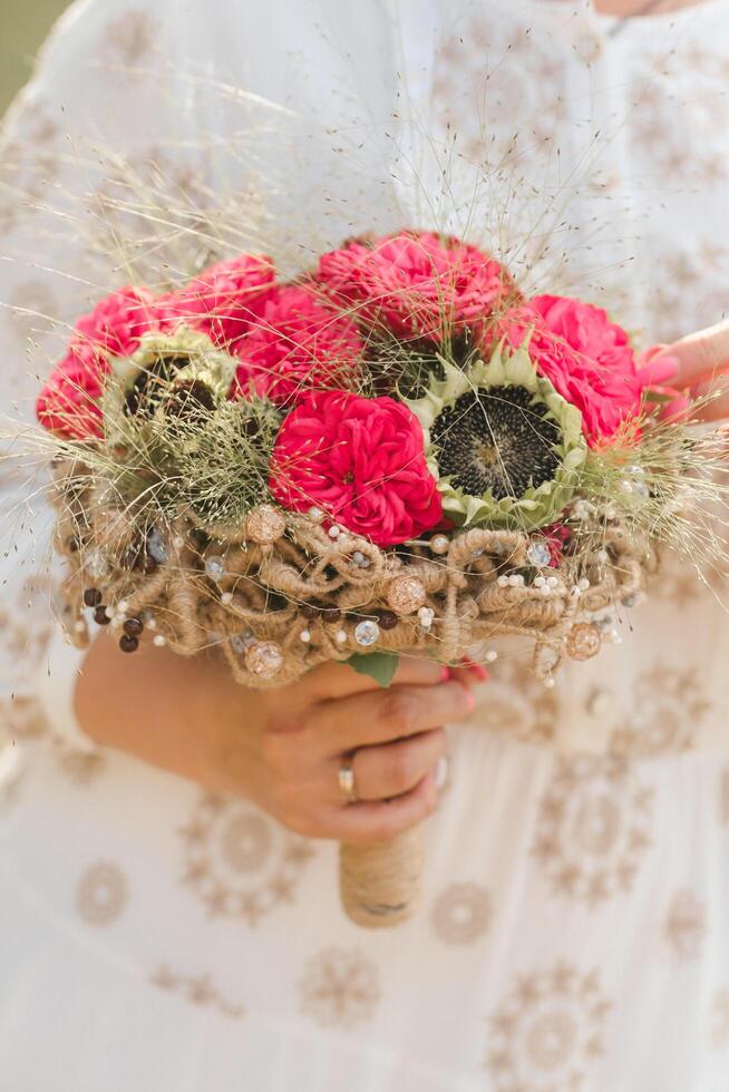 The bride holds her wedding bouquet with red peonies and sunflowers in her hands photo