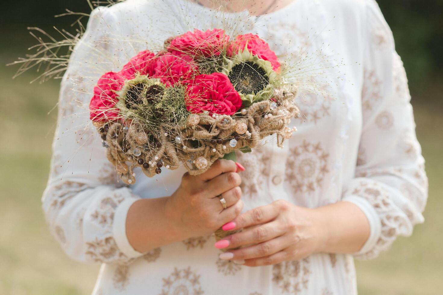 The bride holds her wedding bouquet with red peonies and sunflowers in her hands photo