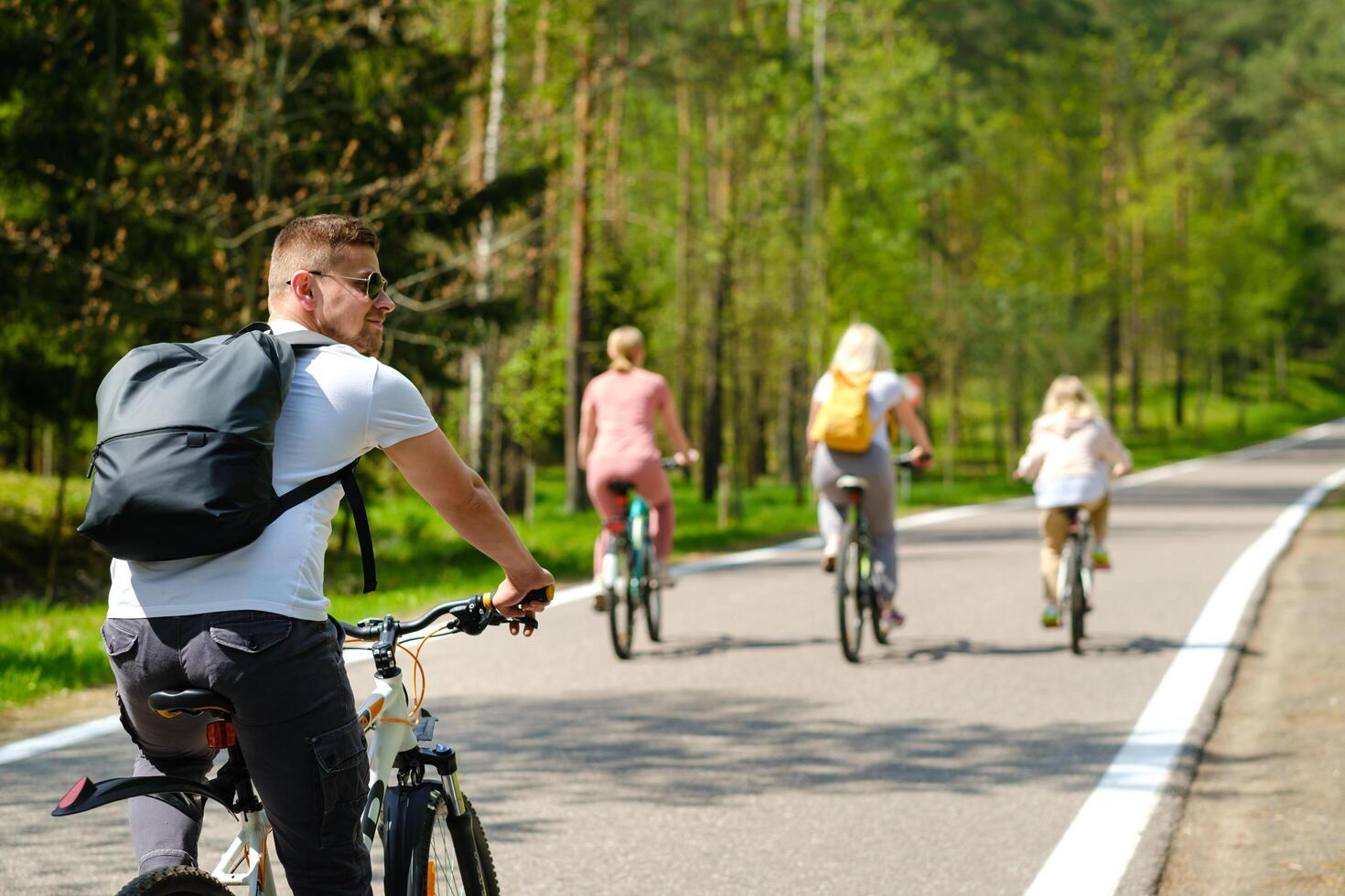 A group of cyclists with backpacks ride bicycles on a forest road enjoying nature photo