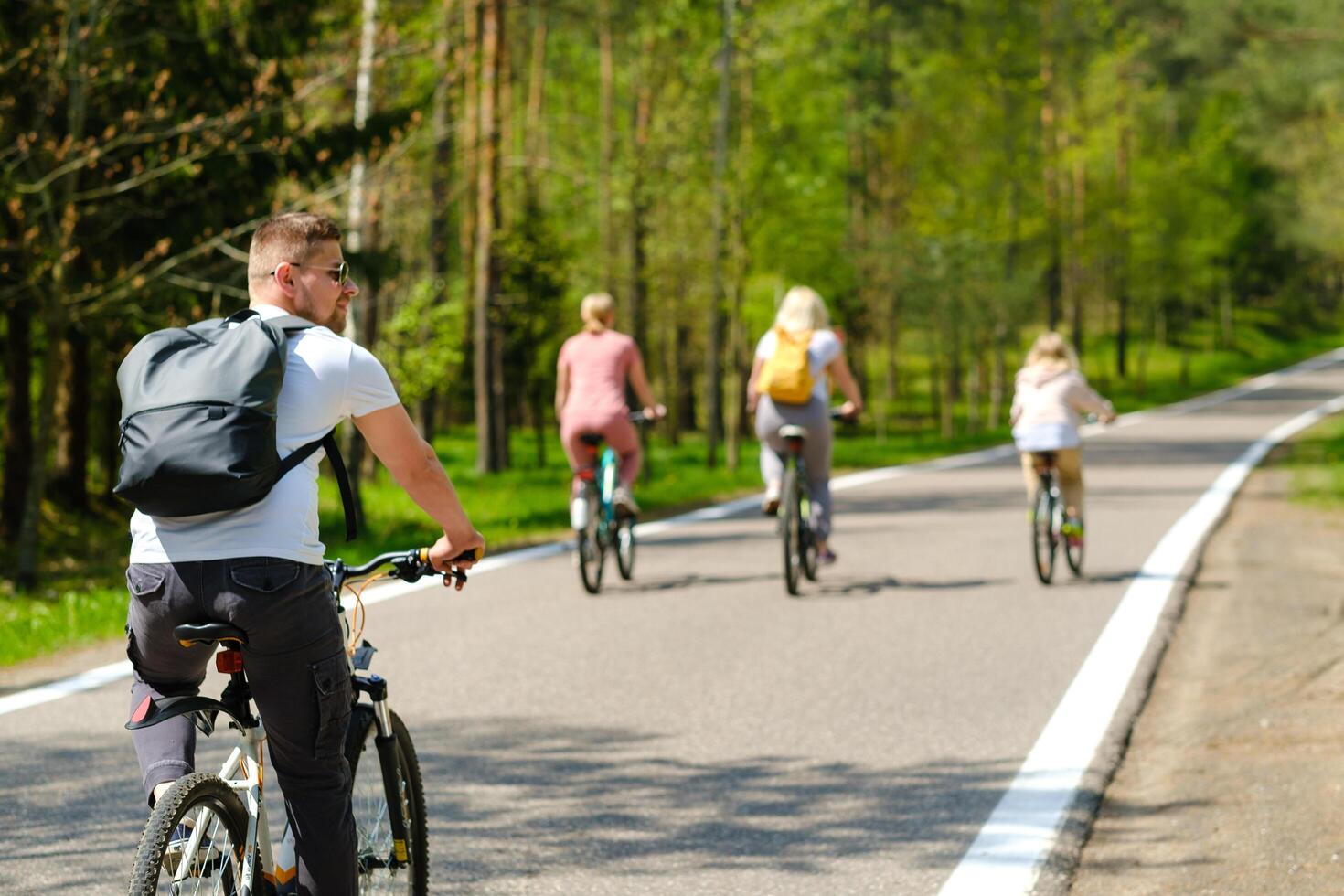 A group of cyclists with backpacks ride bicycles on a forest road enjoying nature photo