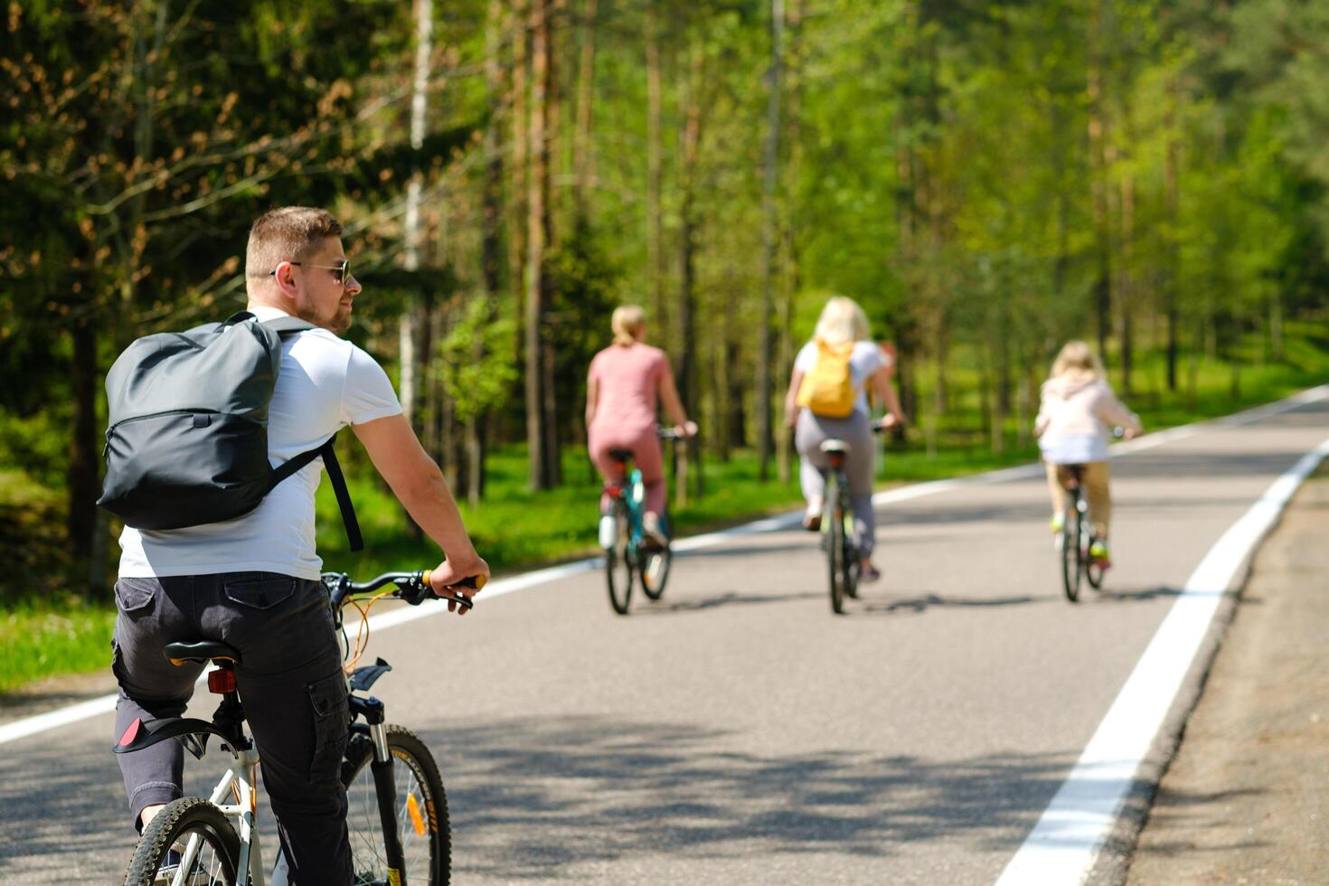 A group of cyclists with backpacks ride bicycles on a forest road enjoying nature photo
