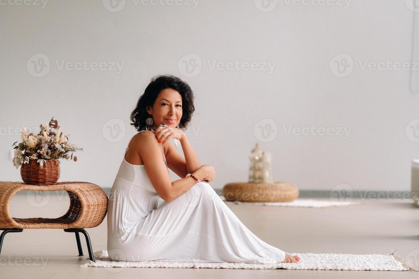 a woman in a white sundress in a bright interior is sitting on a white rug. The concept of relaxation photo
