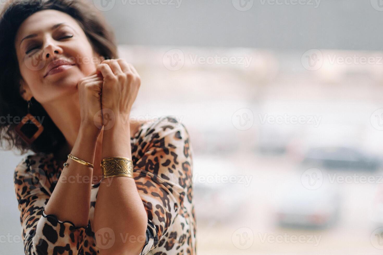 a brunette woman in a tiger dress stands near a large window photo