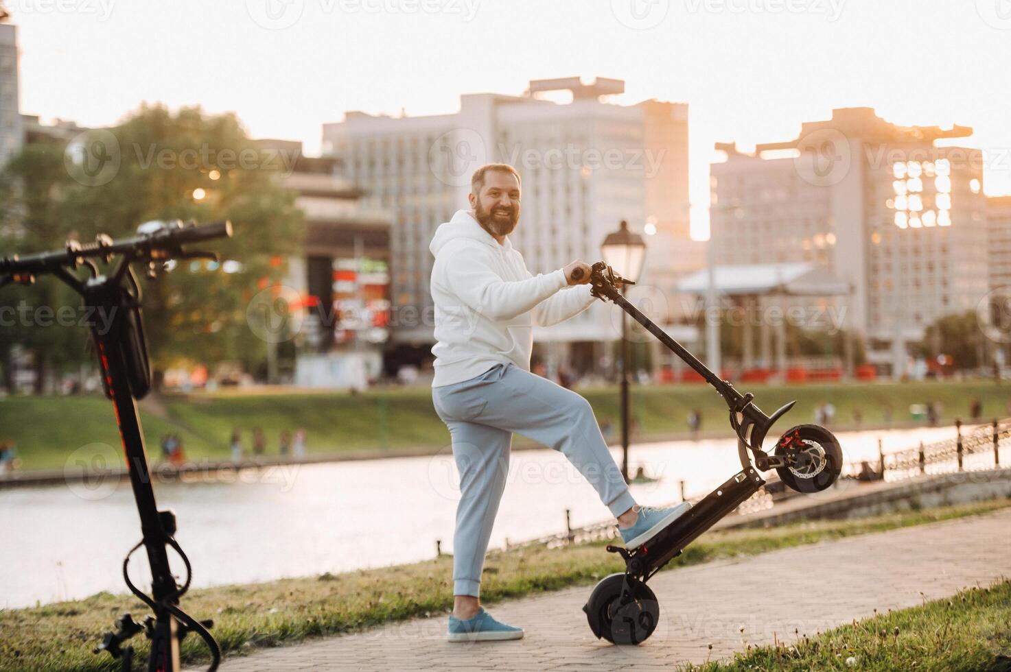 A man with a beard in white clothes rides around the city on an electric scooter at sunset photo