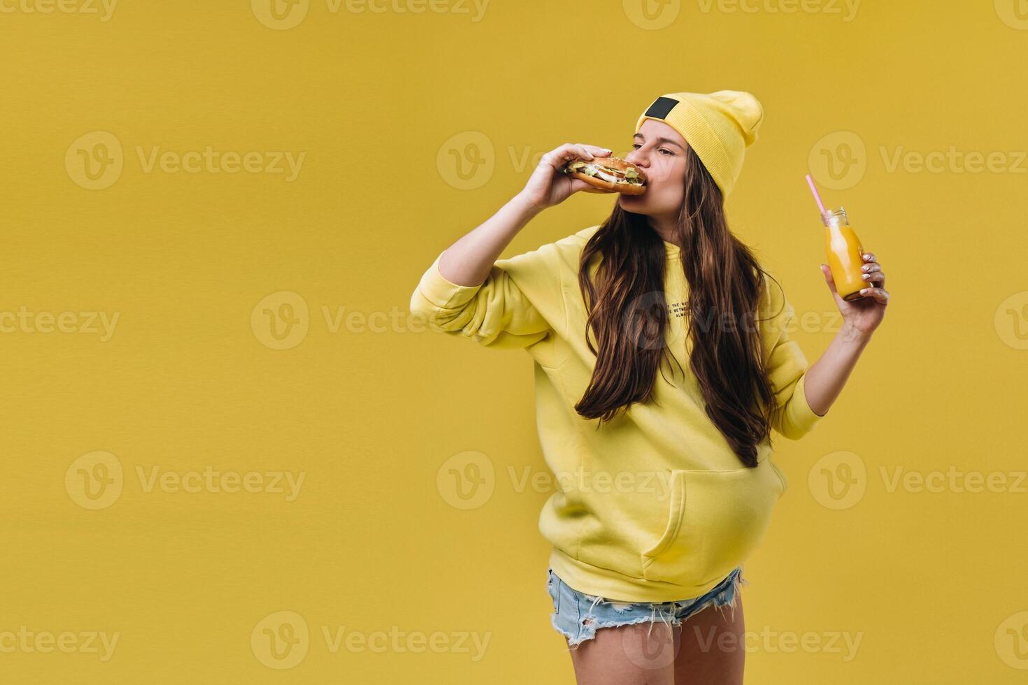 pregnant girl in yellow clothes with hamburgers in her hands on a yellow background photo