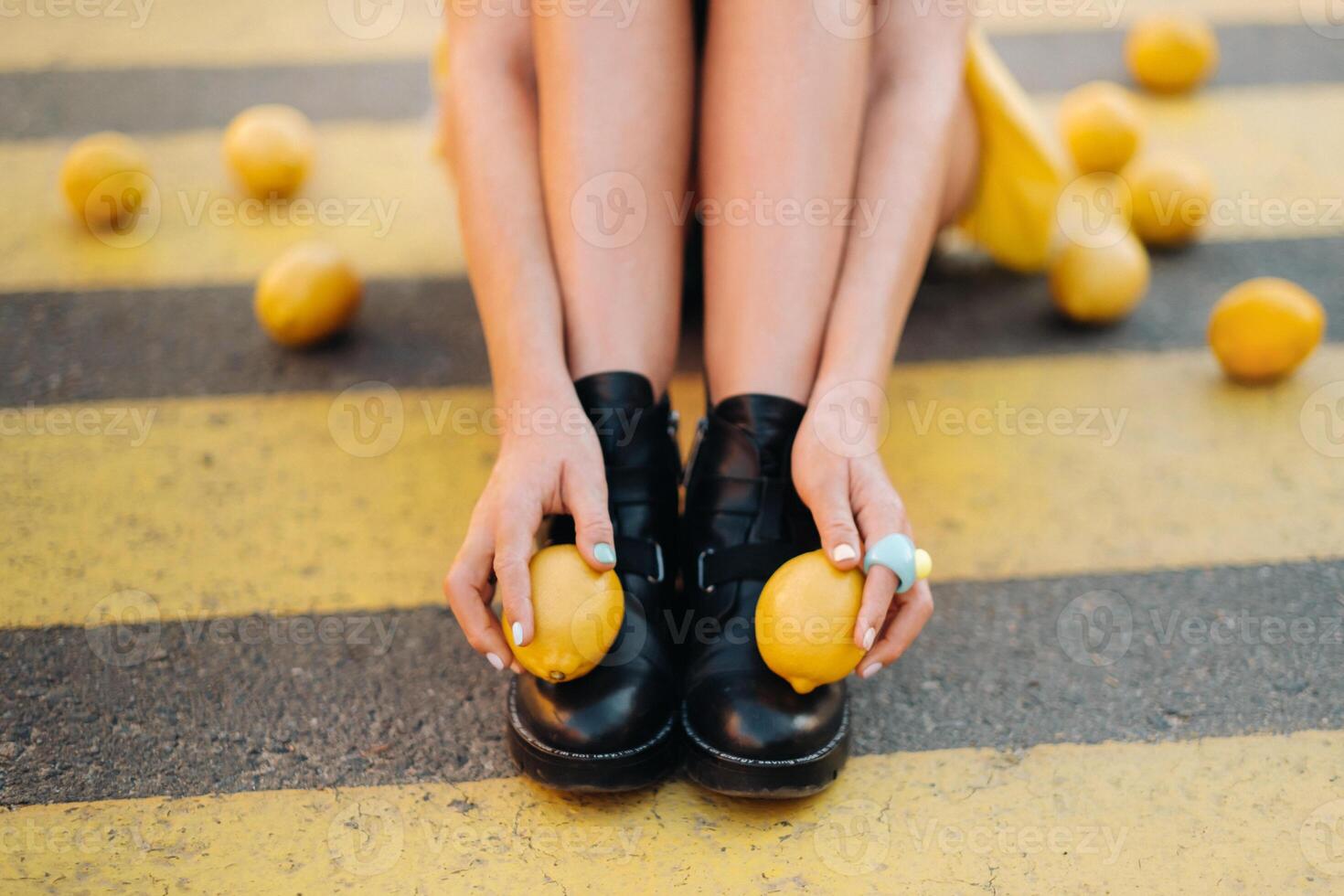 a girl with lemons in a yellow shirt, shorts and black shoes sits on a yellow pedestrian crossing in the city. The lemon mood photo