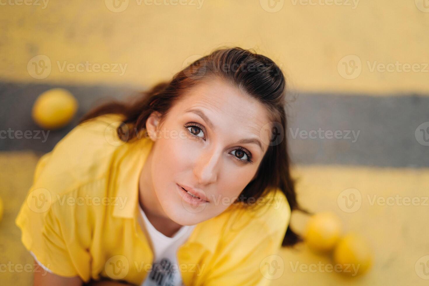 a girl with lemons in a yellow shirt, shorts and black shoes sits on a yellow pedestrian crossing in the city. The lemon mood photo