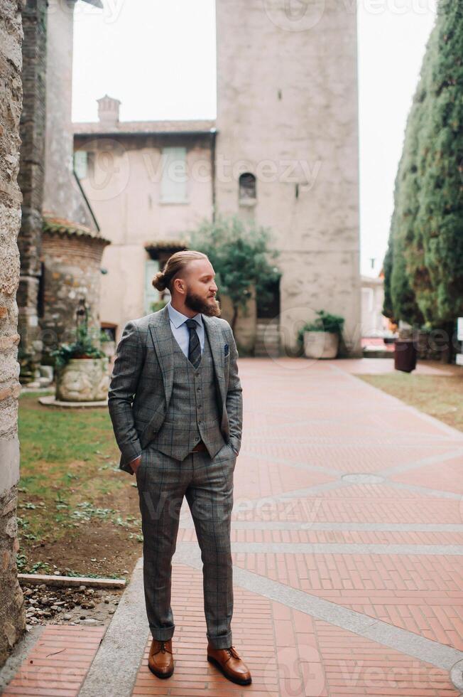 A man with a beard in a strict grey three-piece suit with a tie in the old town of Sirmione, a Stylish man in a grey suit in Italy photo